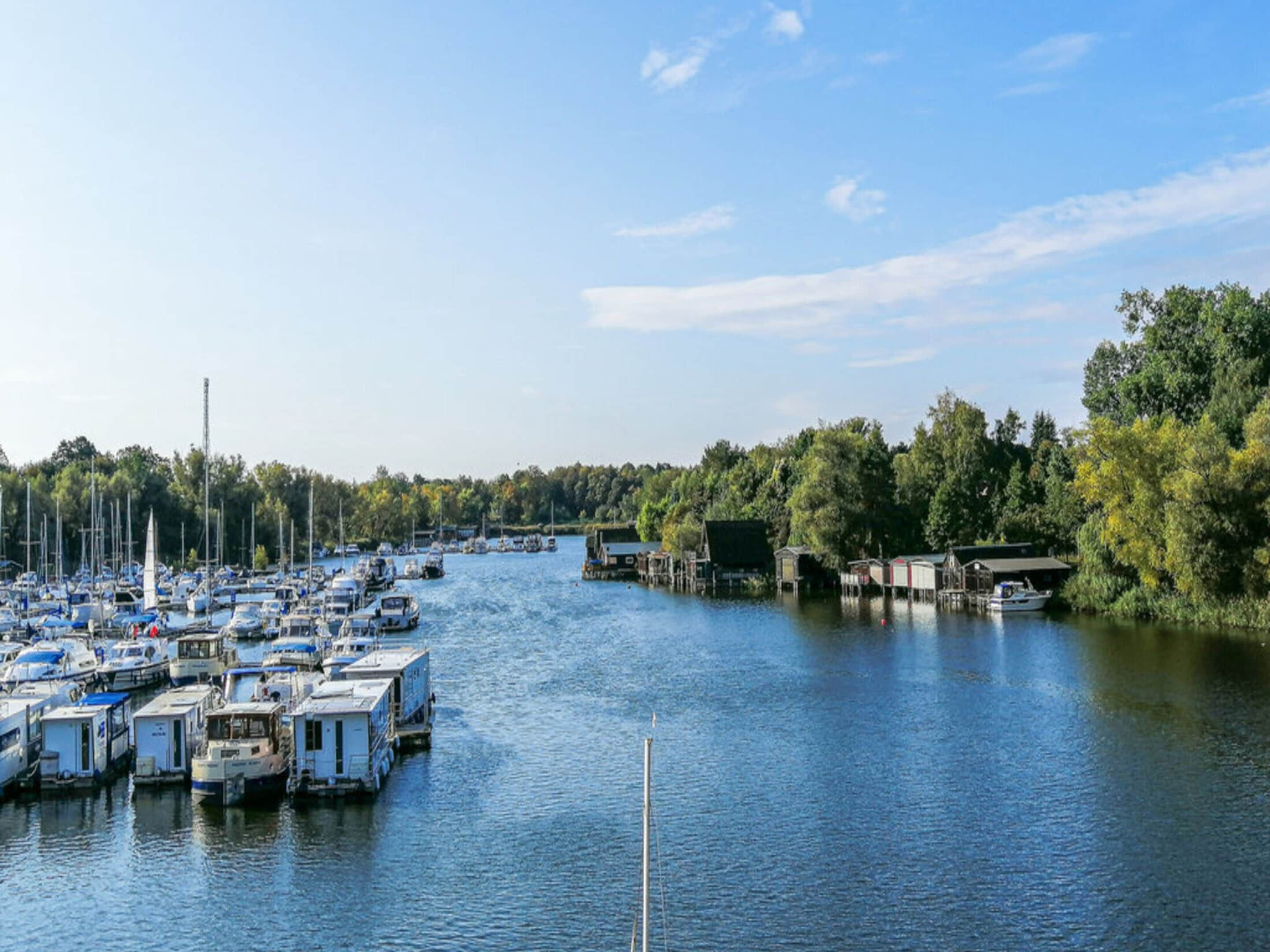 A marina with numerous boats docked along a river, surrounded by trees and greenery.