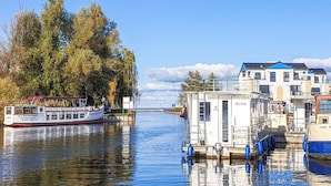 En flod med en båt förtöjd på vänster sida och en liten byggnad med skylten ”RECHLIN” på höger sida.