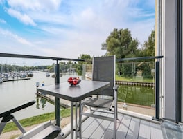 A balcony with a table and chairs, overlooking a marina with boats and a river.