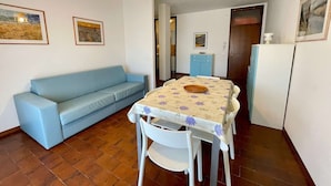 Ein Essbereich mit Tisch, Stühlen, einem blauen Sofa, einer Hängeleuchte und einem Kühlschrank.
