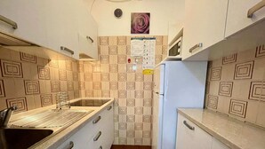 Eine kleine Küche mit Spüle, Herd und Kühlschrank, mit gemusterten Fliesen und einer Wanduhr.