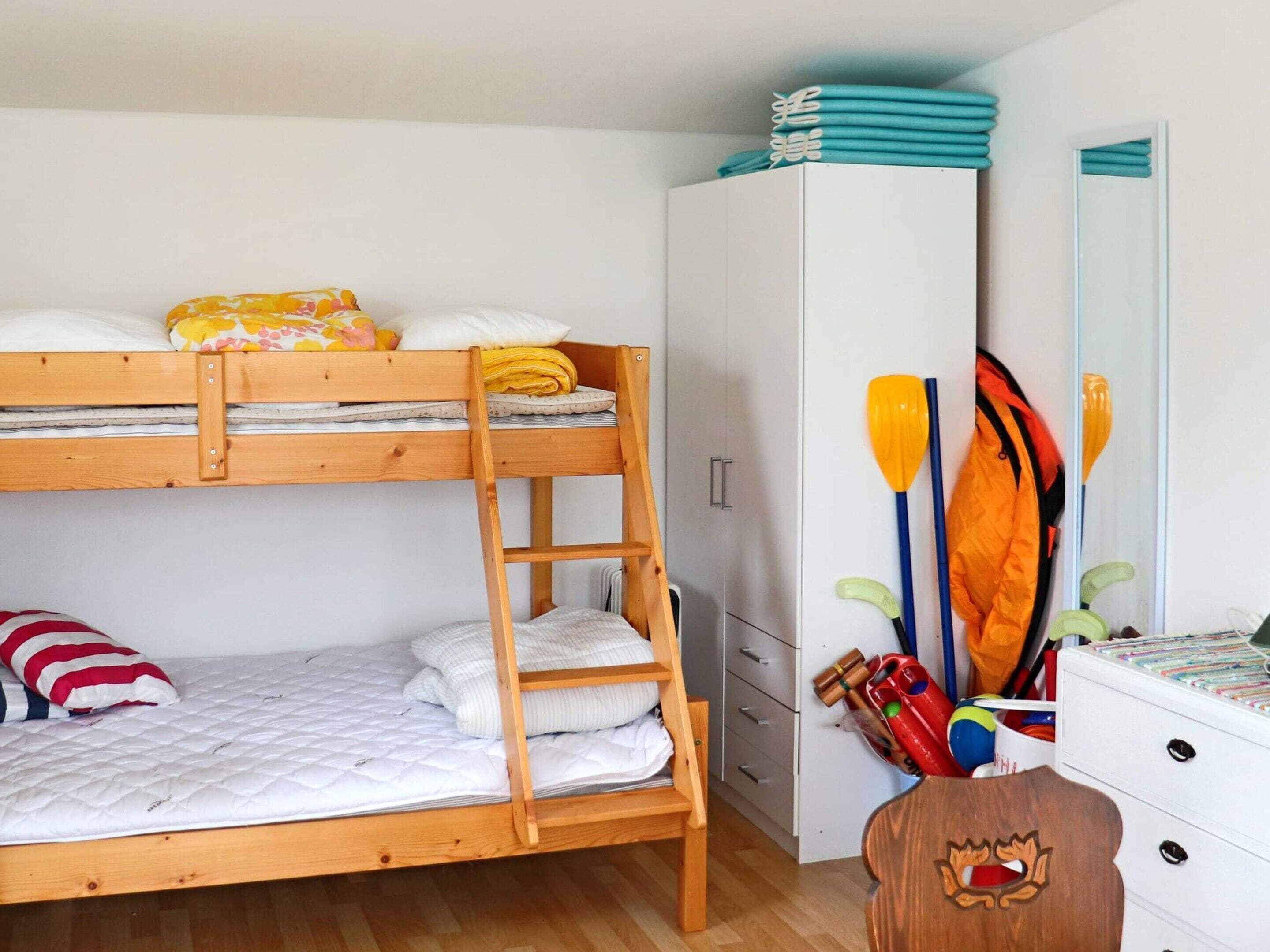 A bunk bed with a ladder, a wardrobe, and a dresser with paddles and a jacket.