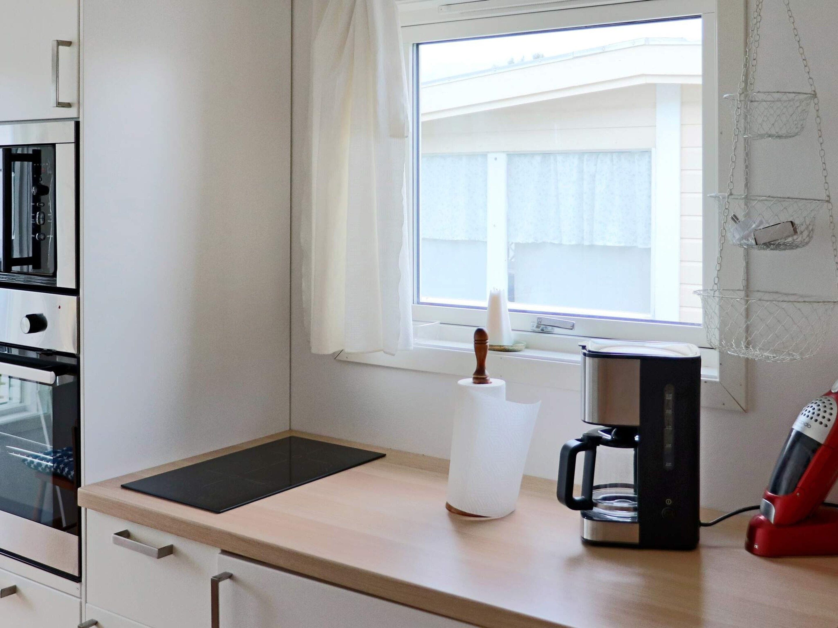 Una kitchenette equipada con microondas, cafetera y una ventana con cortinas.