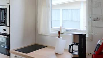 Una kitchenette equipada con microondas, cafetera y una ventana con cortinas.