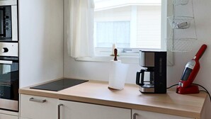 A kitchen with a countertop, a coffee maker, a red electric kettle, and a window with blinds. - 4 Person Holiday Home in Falkenberg (Falkenberg)