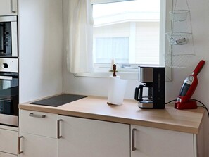 A kitchen with a countertop, a coffee maker, a red electric kettle, and a window with blinds. - 4 Person Holiday Home in Falkenberg (Falkenberg)