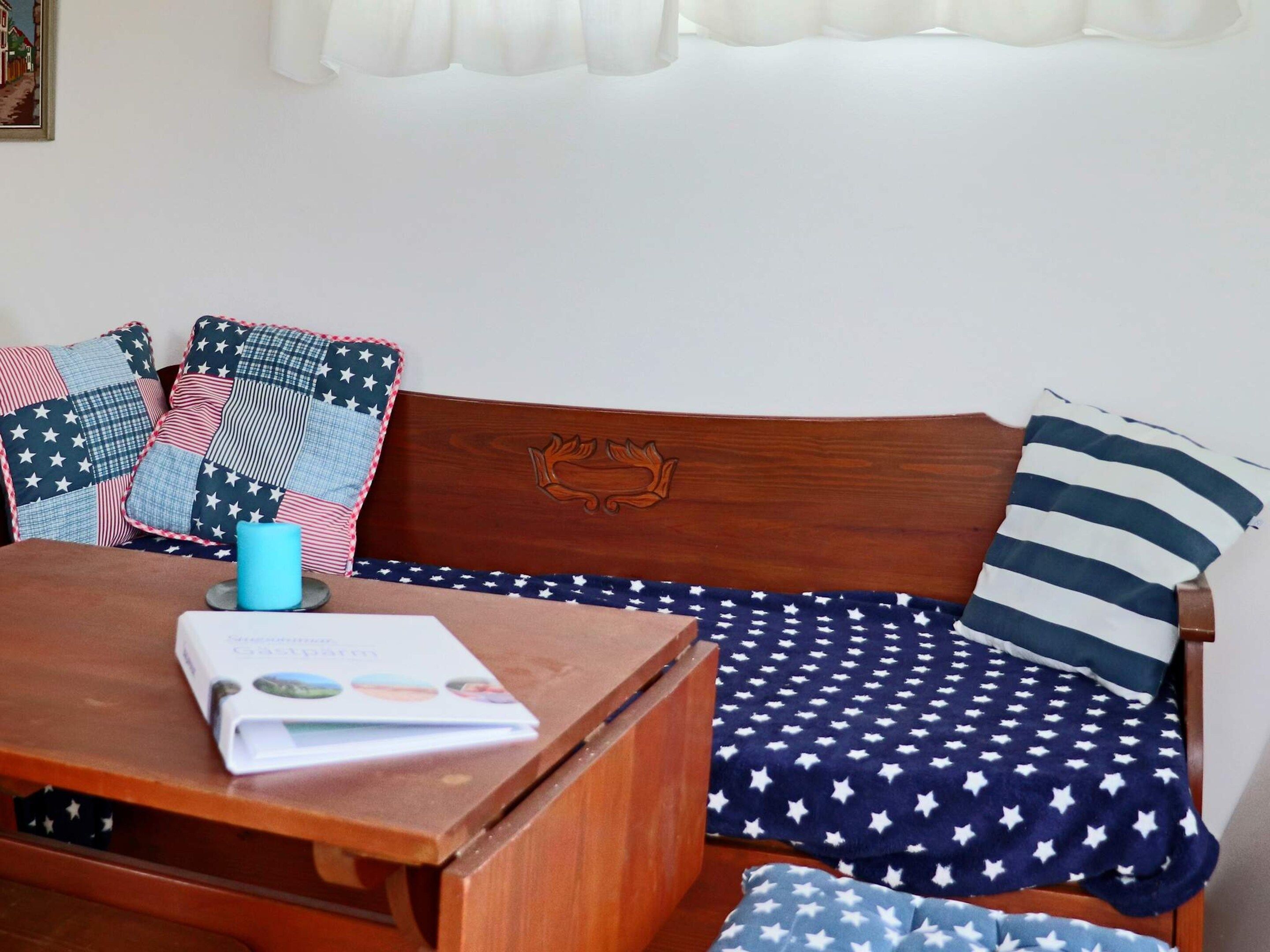 A wooden bench with a cushion featuring a star pattern, a blue mug, and a book on a table.