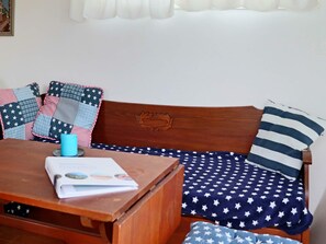 A wooden bench with a cushion featuring a star pattern, a blue mug, and a book on a table. - 4 Person Holiday Home in Falkenberg (Falkenberg)