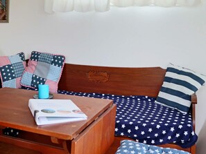 A wooden bench with a cushion featuring a star pattern, a blue mug, and a book on the bench. - 4 Person Holiday Home in Falkenberg (Falkenberg)