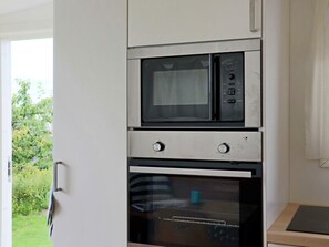 A kitchen with a built-in microwave and oven, a door with a handle, and a view of greenery outside.
