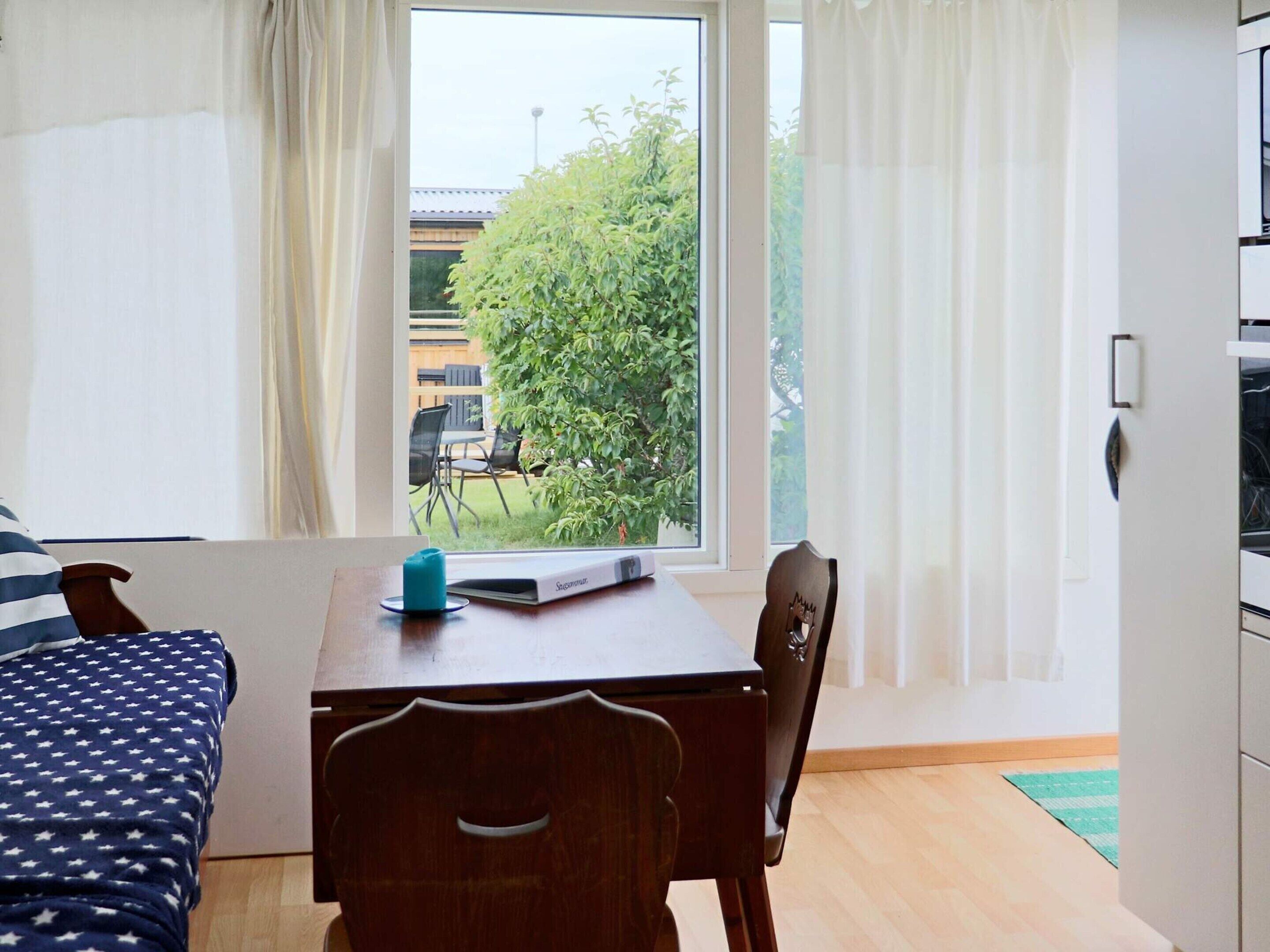 Una habitación con una cama, una mesa con un control remoto, una silla y una ventana con cortinas.