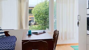 Una habitación con una cama, una mesa con un control remoto, una silla y una ventana con cortinas.