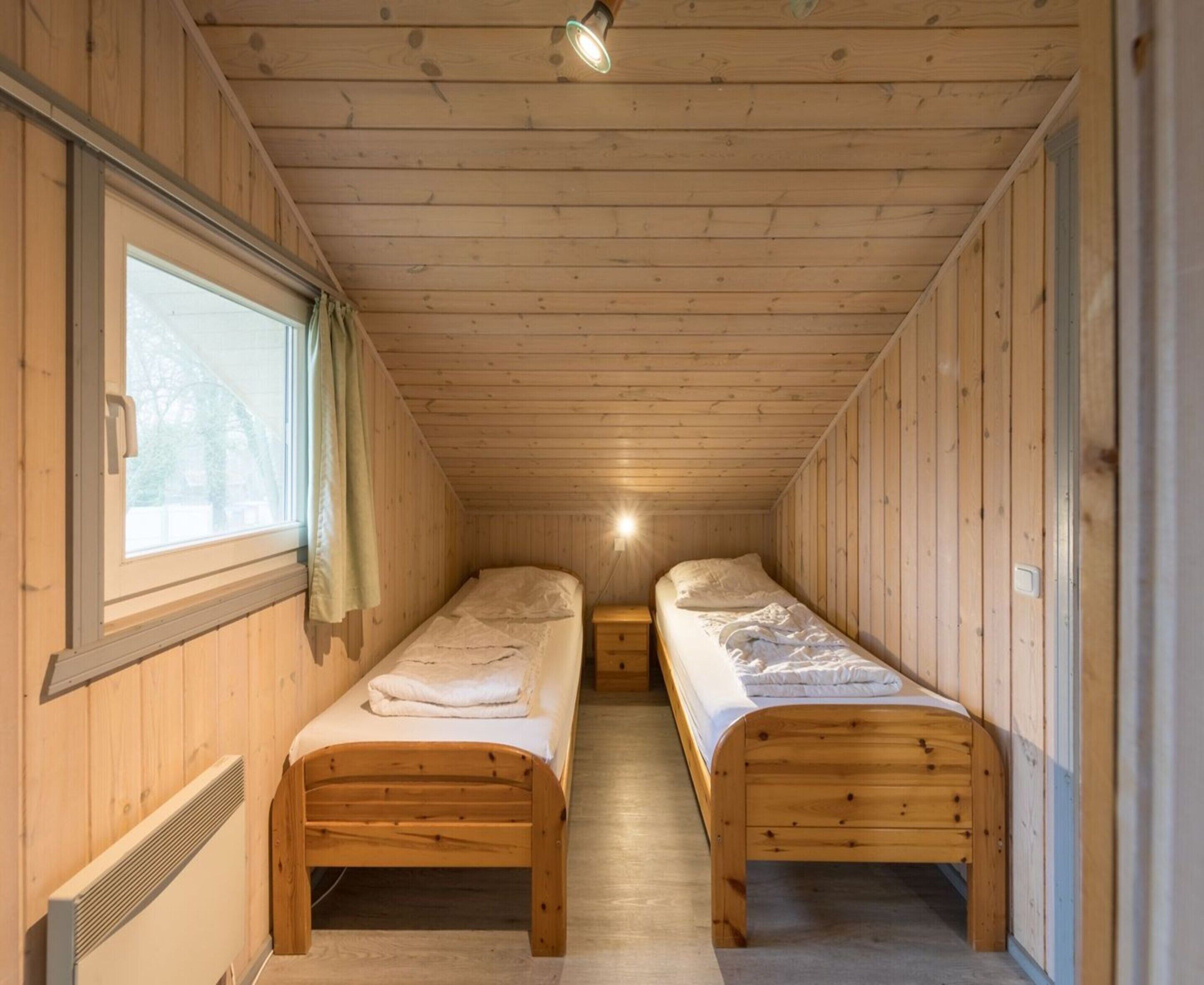 Una piccola baita di legno con due letti singoli, una finestra e una luce a soffitto.