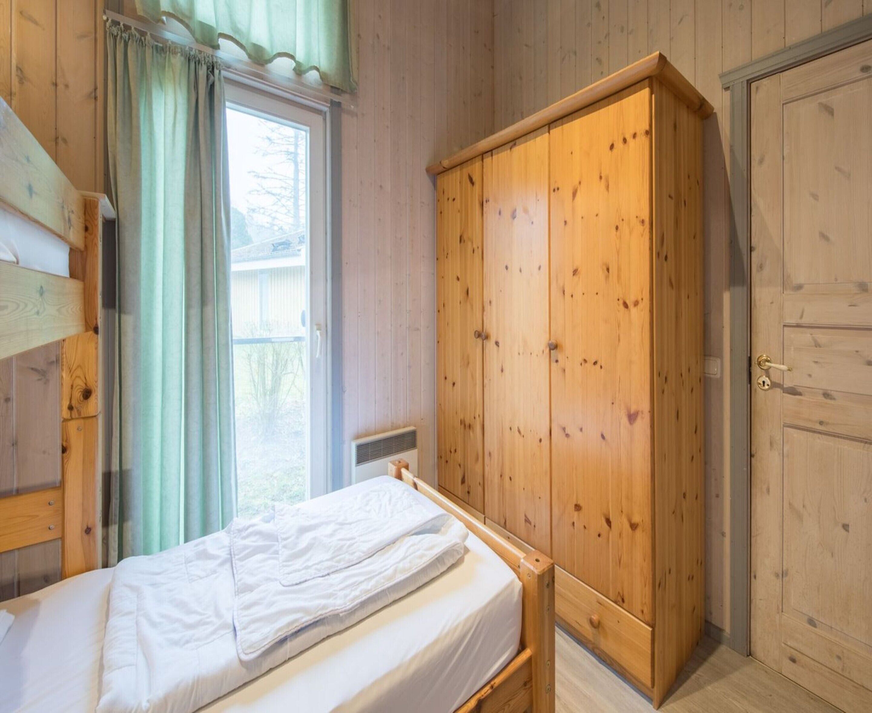 Une pièce en bois avec un lit, une armoire et une fenêtre avec des rideaux.