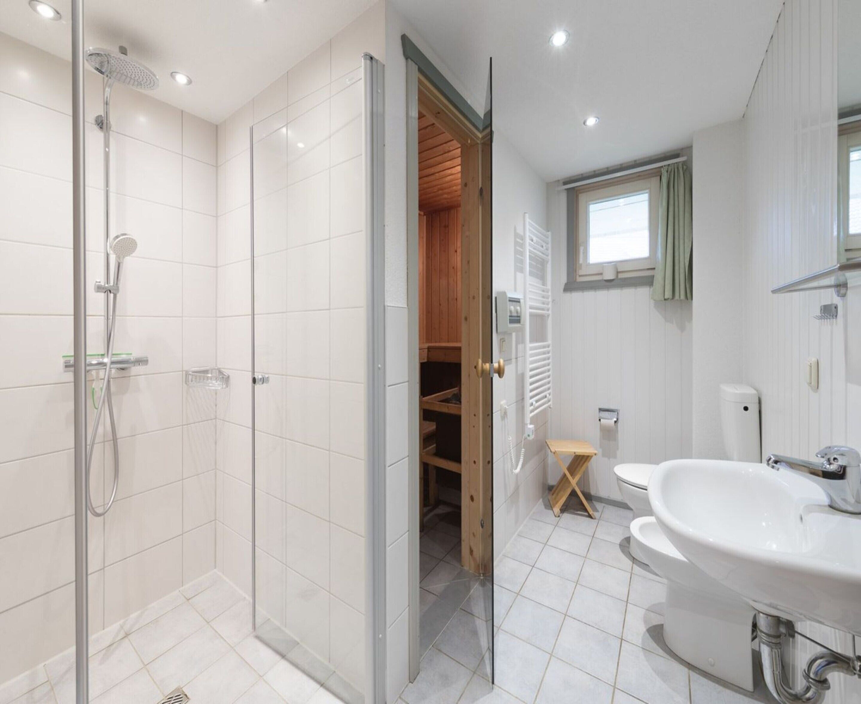 Un baño moderno con ducha envuelta en vidrio, armario de madera y lavamanos blanco.