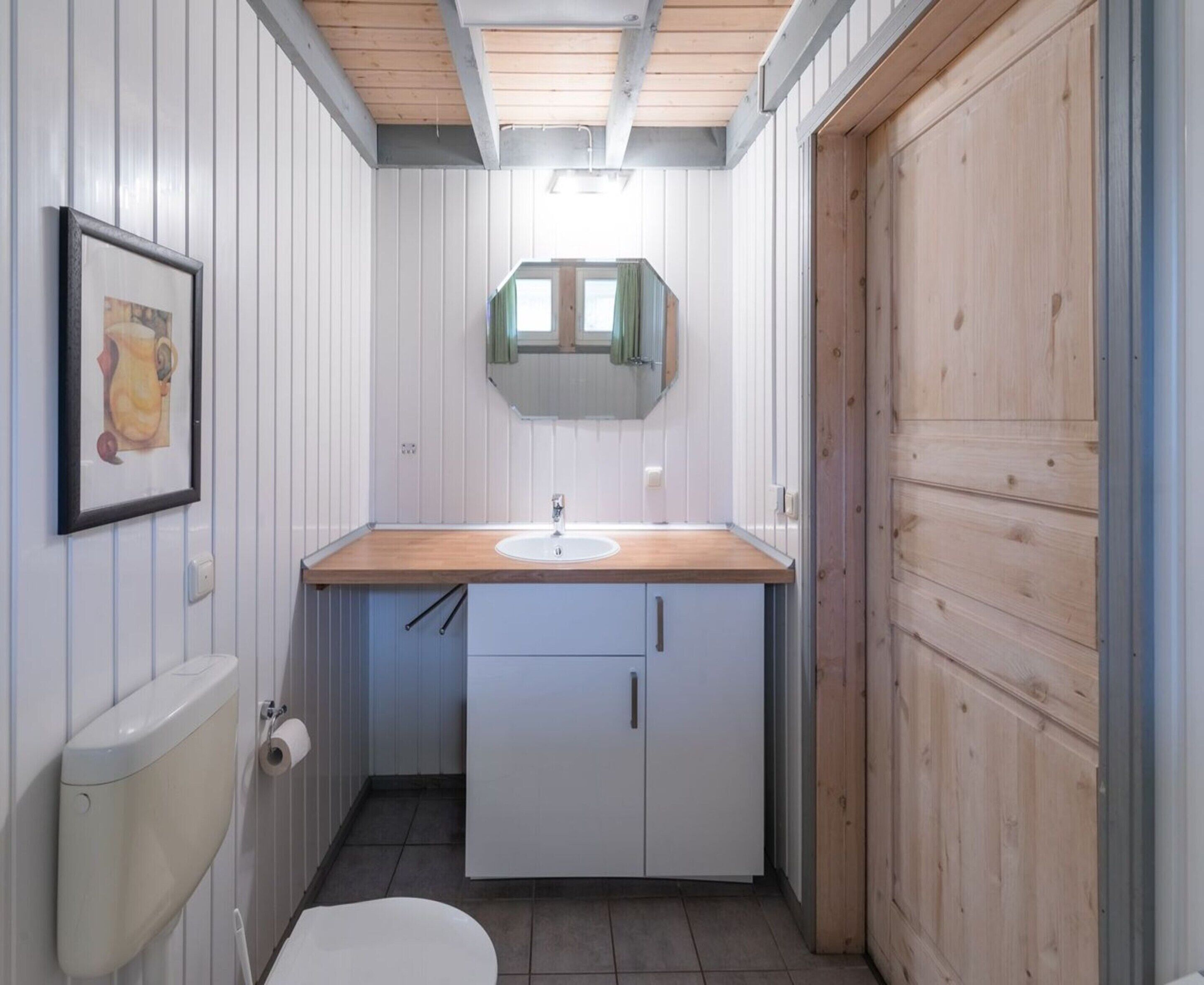 A compact bathroom with a wooden vanity, a toilet, and a mirror above the sink.