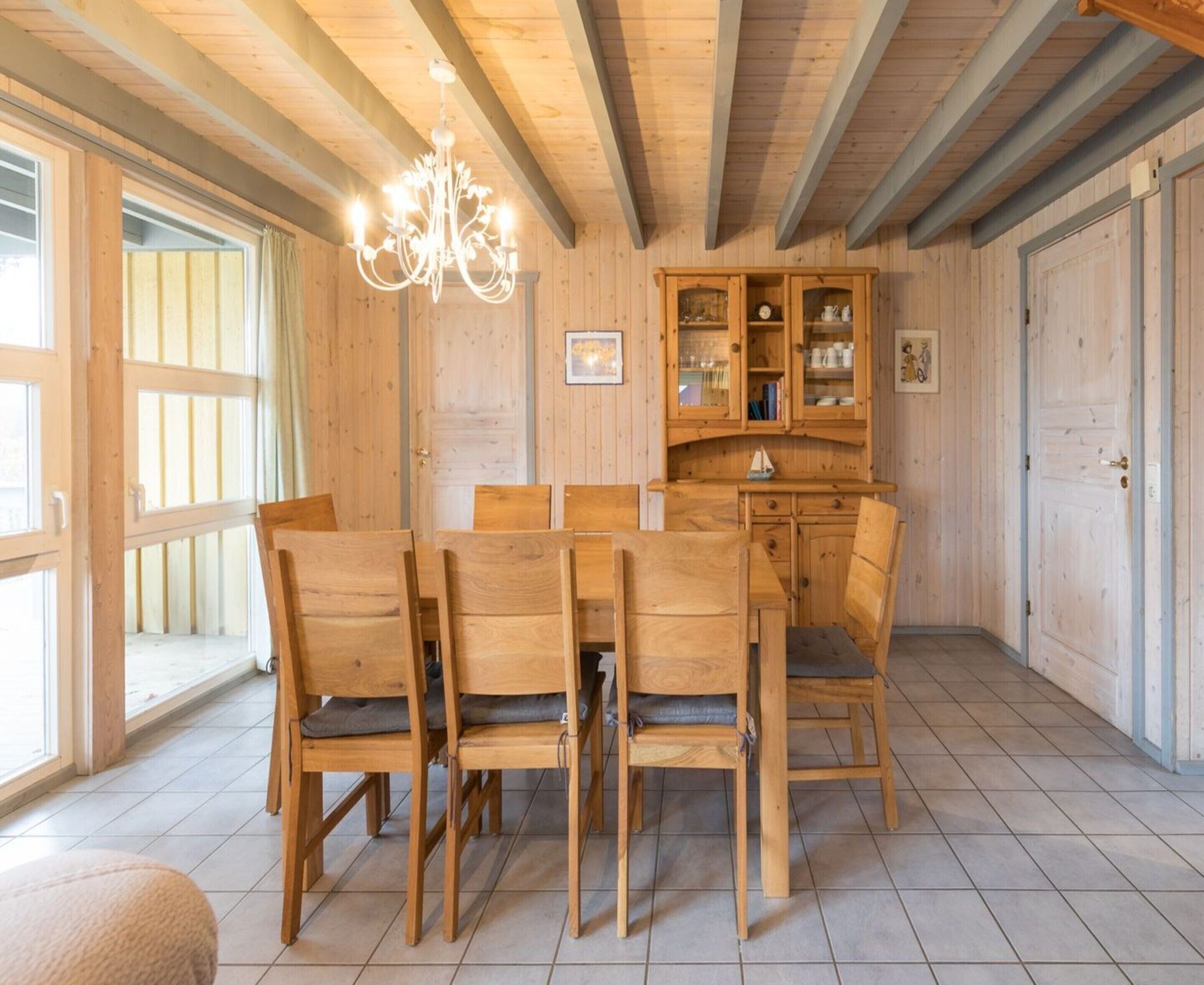 A wooden dining room with a chandelier, wooden chairs, a table, and cabinets.