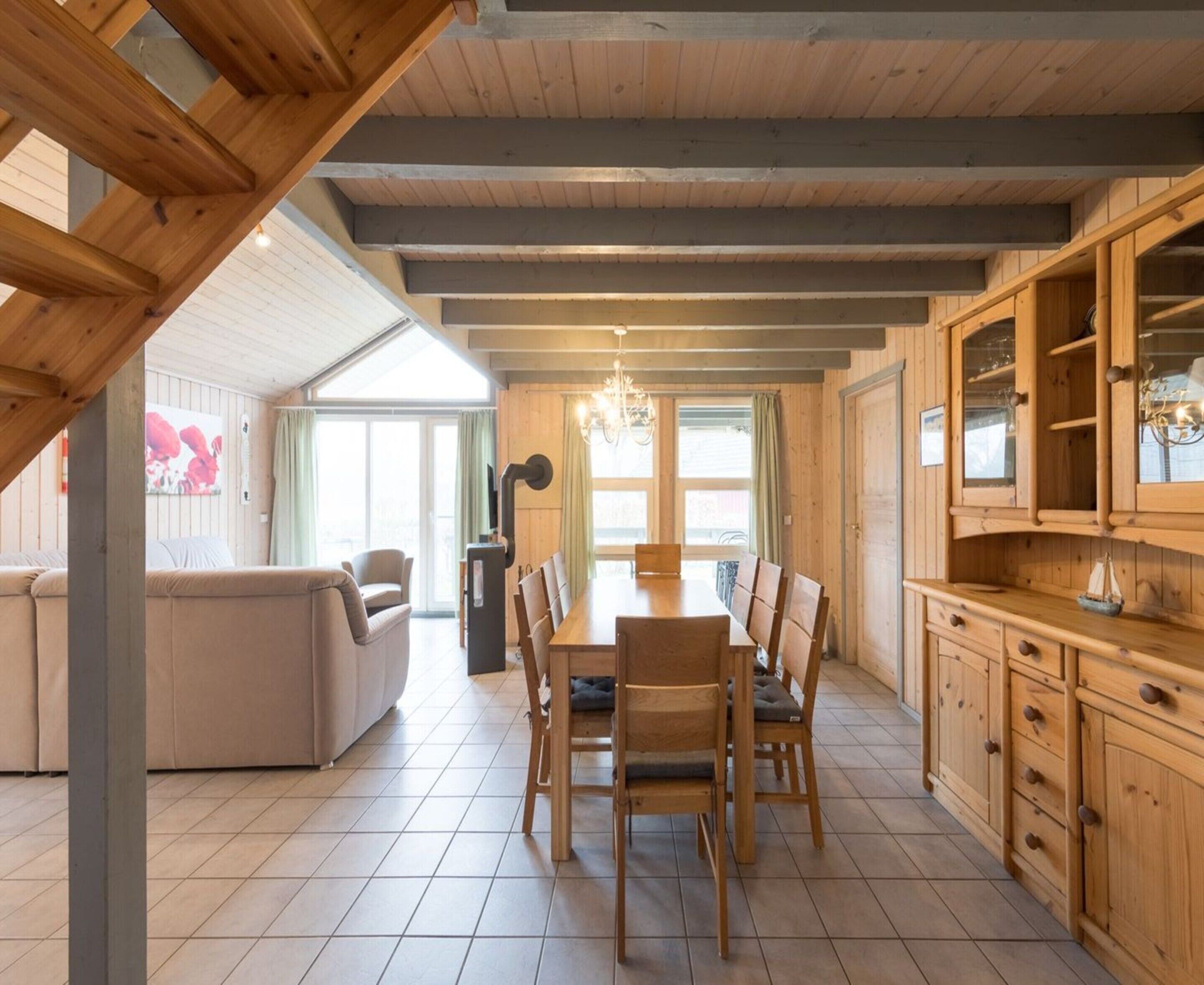 A spacious dining area with a wooden table and chairs, a sofa, and a kitchen area with wooden cabinets.