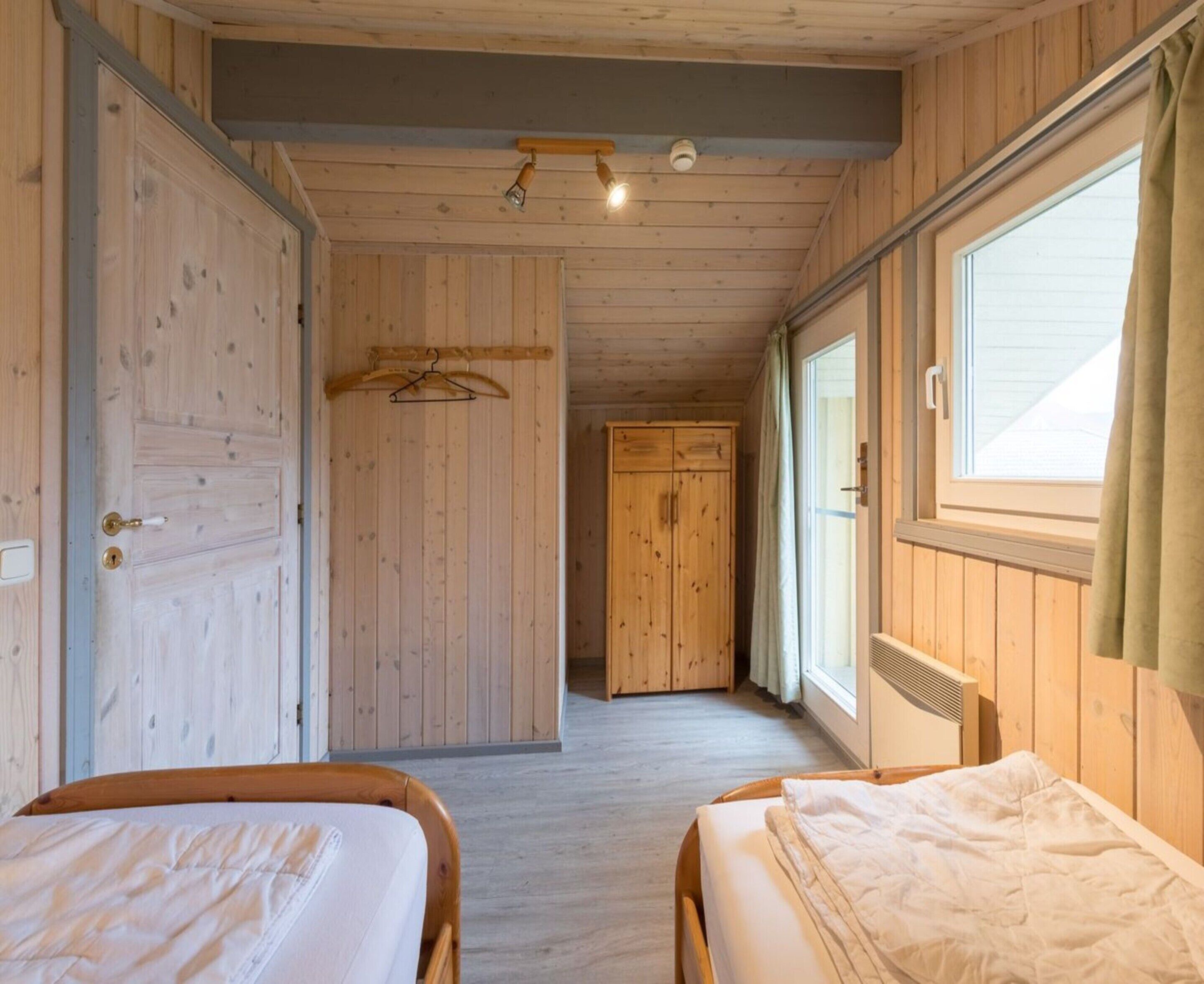 Ein Zimmer mit zwei Betten, Holzwänden, einem Flur und einem Fenster mit Vorhängen.