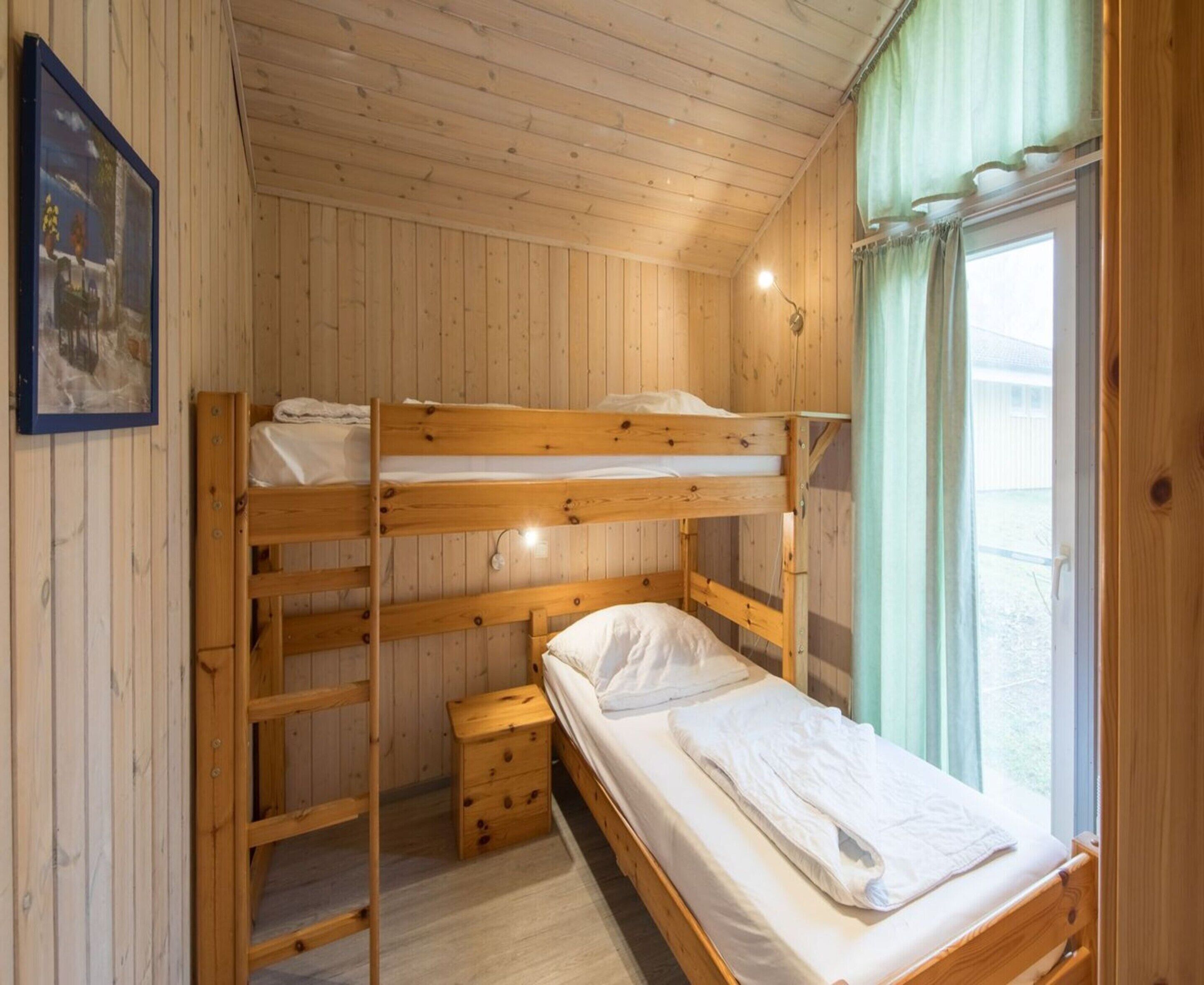 En stuga med träpanel, våningssängar, en liten trälåda och ett fönster med gardiner.