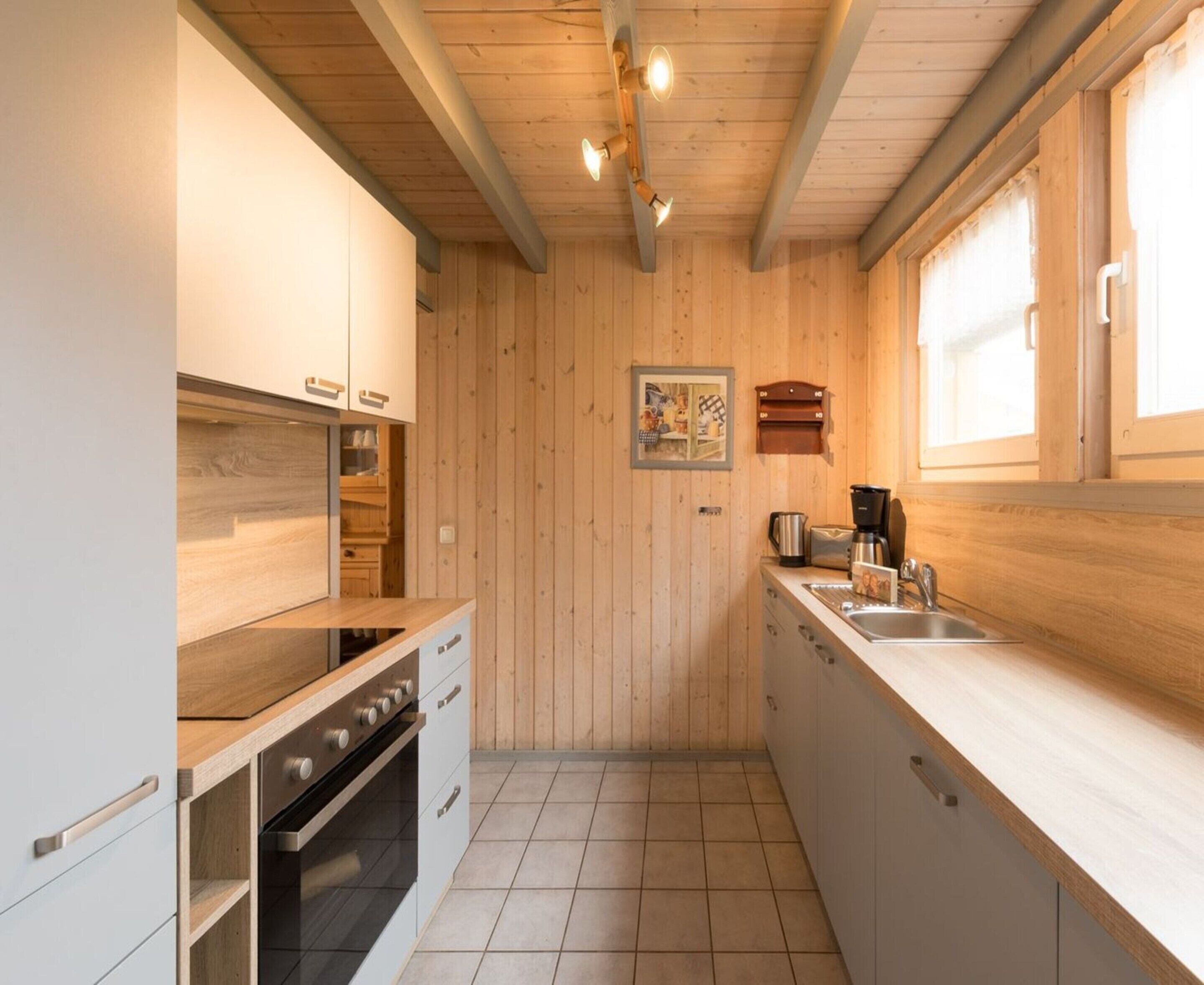 A compact kitchen with wooden walls, a tiled floor, a built-in oven, a sink, and a coffee maker.