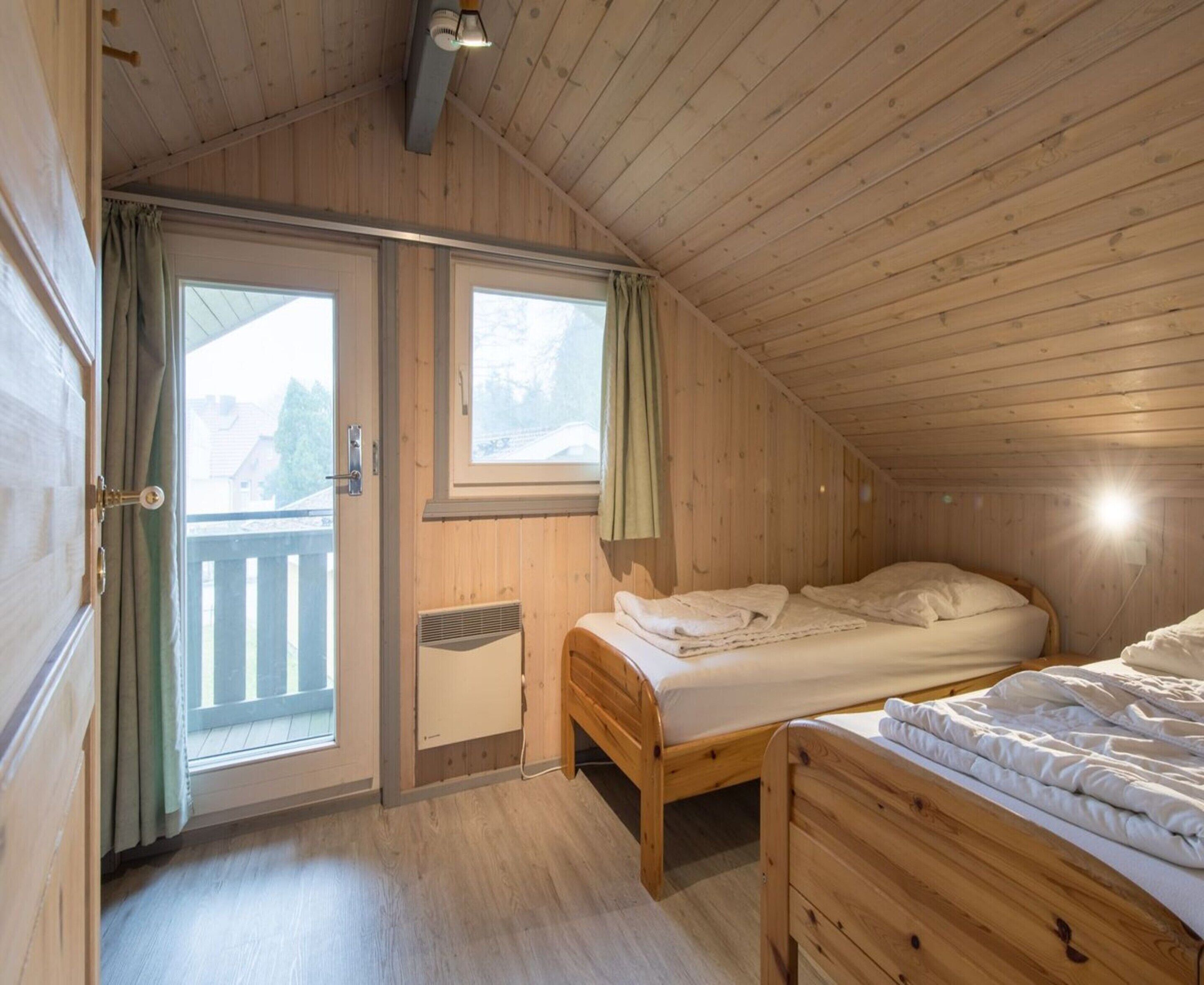 Acogedora habitación tipo cabaña de madera con dos camas, una puerta corrediza de vidrio a un balcón y un pequeño calentador.