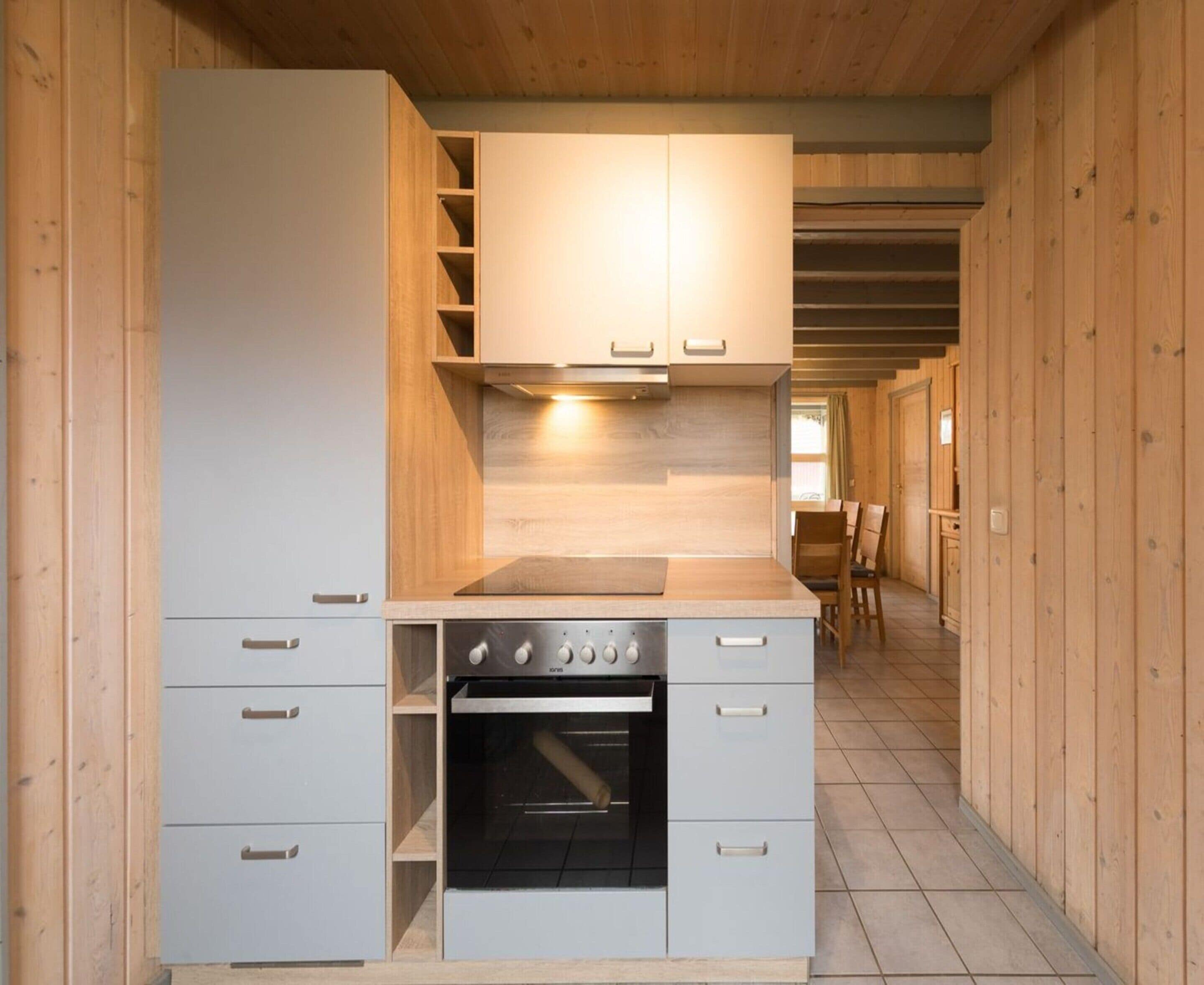 A compact kitchen with white cabinets, a built-in oven, and a wooden ceiling.