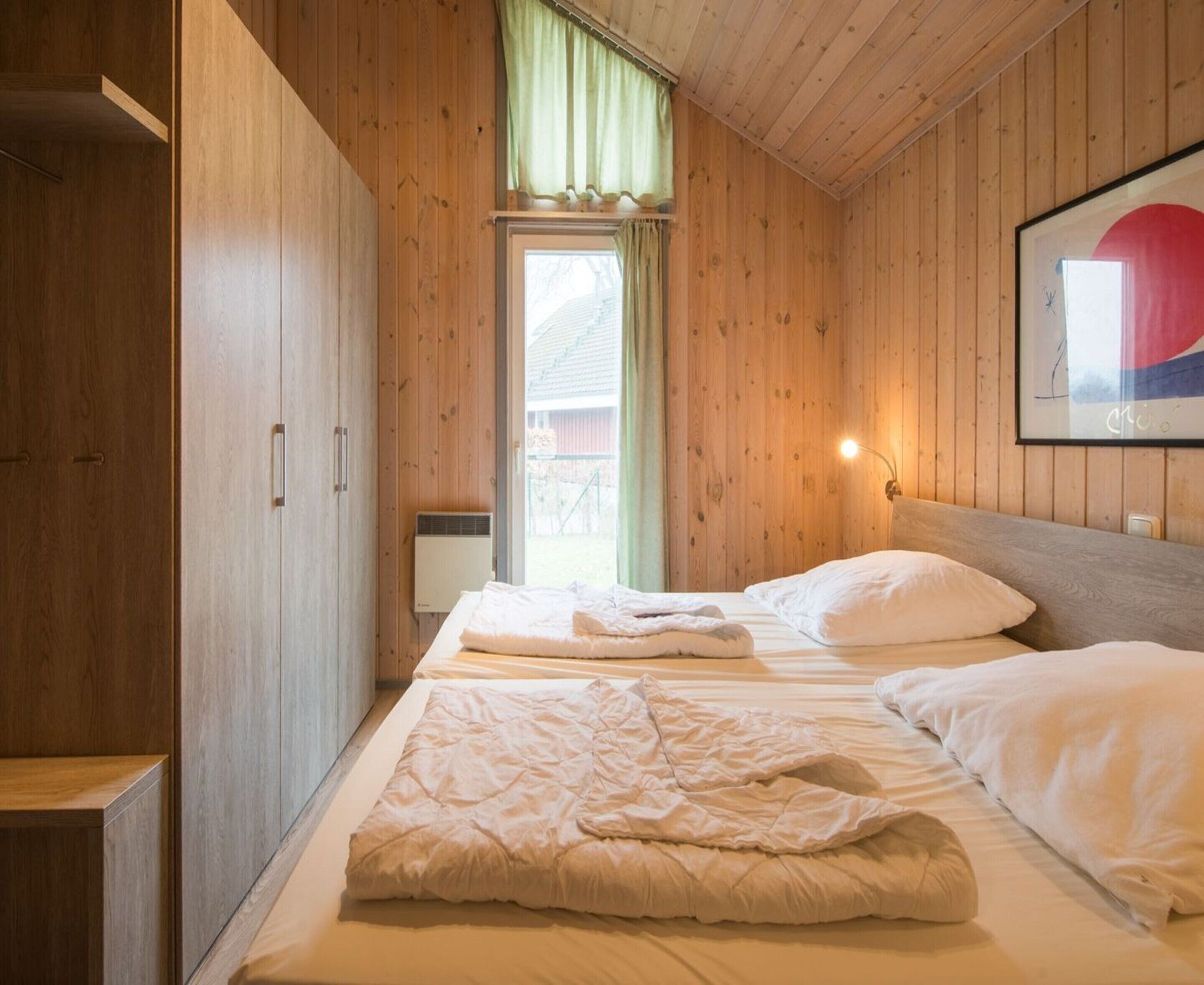 Une chambre avec deux lits, des murs en bois, une fenêtre avec des rideaux et un tableau encadré au mur.