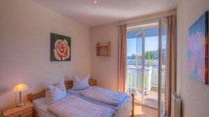 A bedroom with two beds, a nightstand, a painting of a rose, and a view of a balcony with a railing. - Charmante Ferienwohnung (Rechlin)