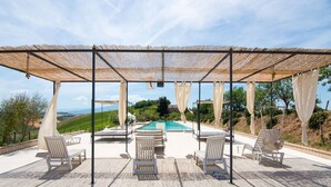 Ein überdachter Außenbereich mit Pool, Liegestühlen und Blick auf die Landschaft.