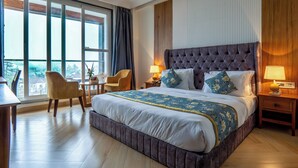 A modern hotel room with a large bed, a sitting area with a chair and table, and a view through large windows. - Xyst Notting Hill (Dehradun)