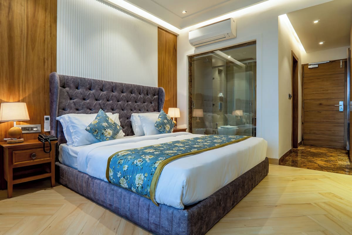 Un grand lit avec une tête de lit capitonnée, une table de chevet en bois avec une lampe et une cabine de douche en verre.