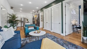 A modern living room with a blue sofa, a round coffee table, and a kitchen in the background. - Crazy Town East Nash Chic Condo Just 13 min to Downtown in East Nash, Great for Groups! (Nashville)