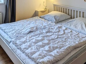 A bed with a white quilted duvet and pillows, a bedside table with a lamp, and a white headboard.