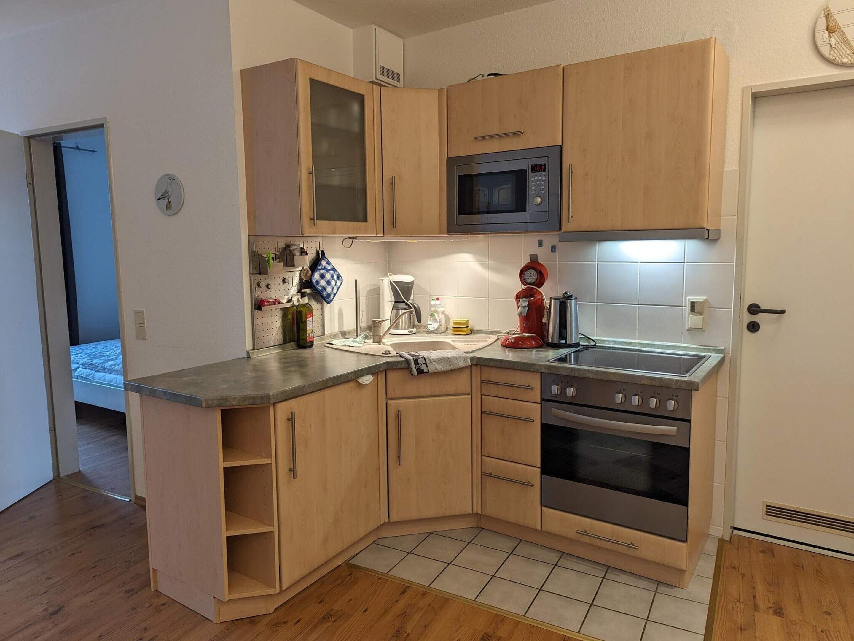 A compact kitchen with wooden cabinets, a microwave, a stove, and a coffee maker.