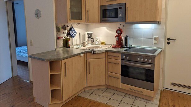 A compact kitchen with wooden cabinets, a microwave, a stove, and a coffee maker. - 4 Star Holiday Home in Neuschonberg (Schönberg)