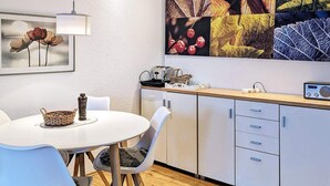 A modern kitchen with white cabinets, a wooden countertop, a dining table with chairs, a radio, and a framed artwork on the wall. - 4 Star Holiday Home in Neuschonberg (Schönberg)