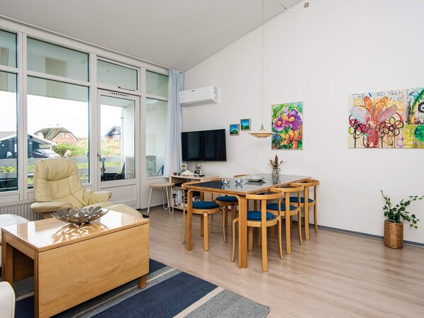 Una sala de estar moderna con sofá, mesa de centro, televisor, mesa de comedor con sillas y obras de arte en las paredes.