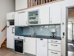A compact kitchen with white cabinetry, a built-in oven, a coffee machine, and a window overlooking a residential area.