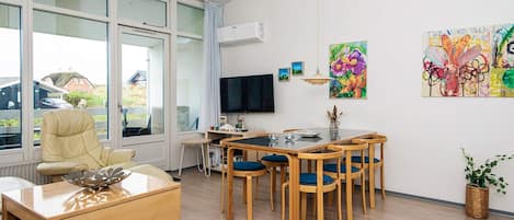 A modern living room with a sofa, coffee table, TV, dining table with chairs, and artwork on the walls.