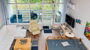 A modern living room with a sofa, a dining table with chairs, a TV, and a balcony with outdoor furniture.