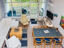 Una sala de estar moderna con un sofá, una mesa de comedor con sillas, un televisor y un balcón con mobiliario exterior.