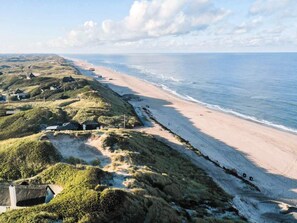 A coastal landscape with a beach and dunes, featuring houses and a lighthouse. - 4 Star Holiday Home in Ringkobing (Ringkobing)