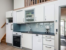 Una kitchenette compacta con gabinetes blancos, horno empotrado, cafetera y microondas.