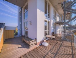 Una terraza de madera con una mesa y sillas, un escape de incendios y un edificio con ventanas grandes.