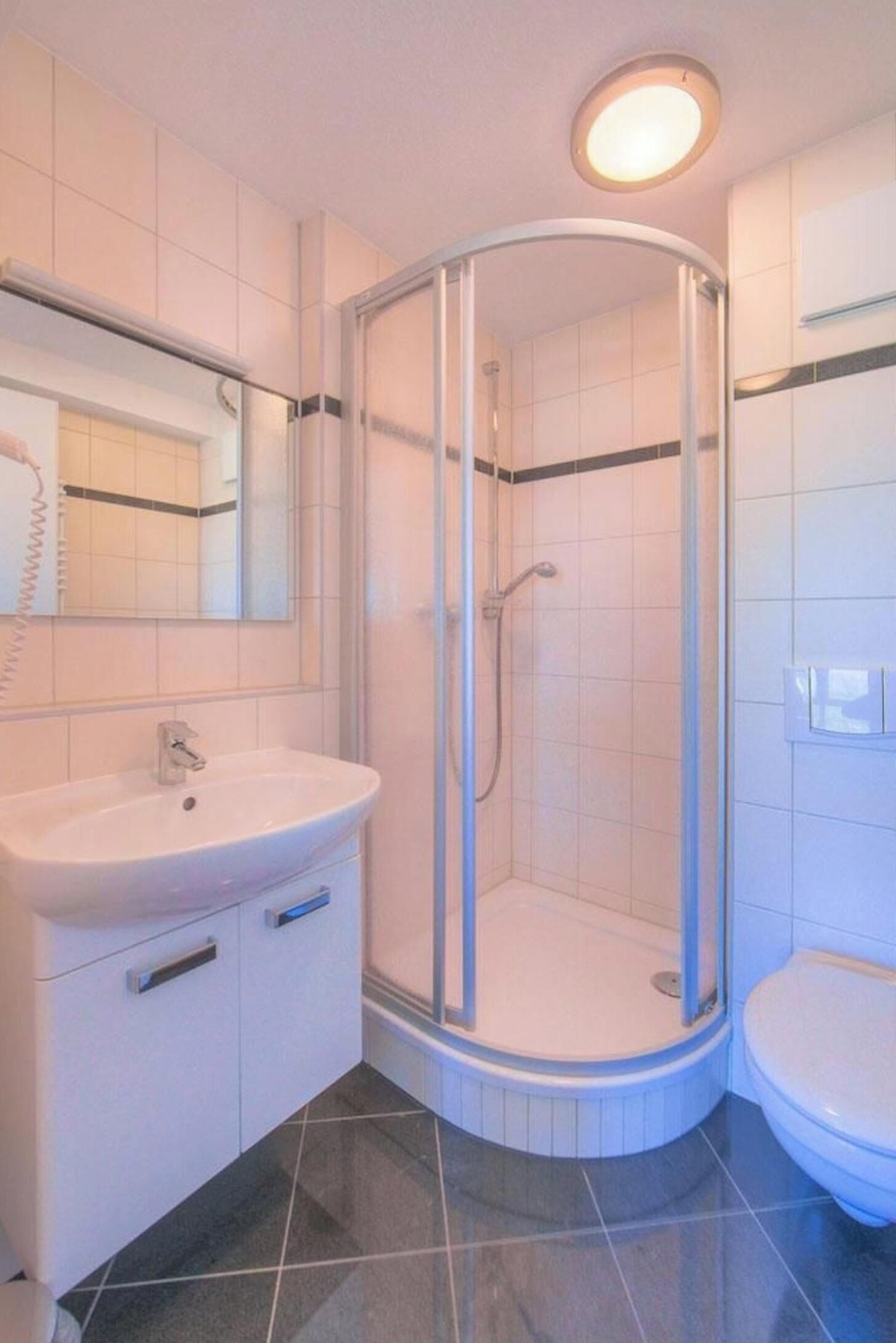 Ein Badezimmer mit Duschkabine, Waschbecken inklusive Spiegel und Toilette.