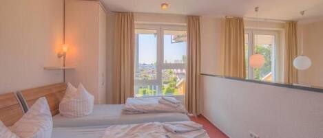 A hotel room with two beds, a large window with curtains, a view of the city, and a wall-mounted lamp.