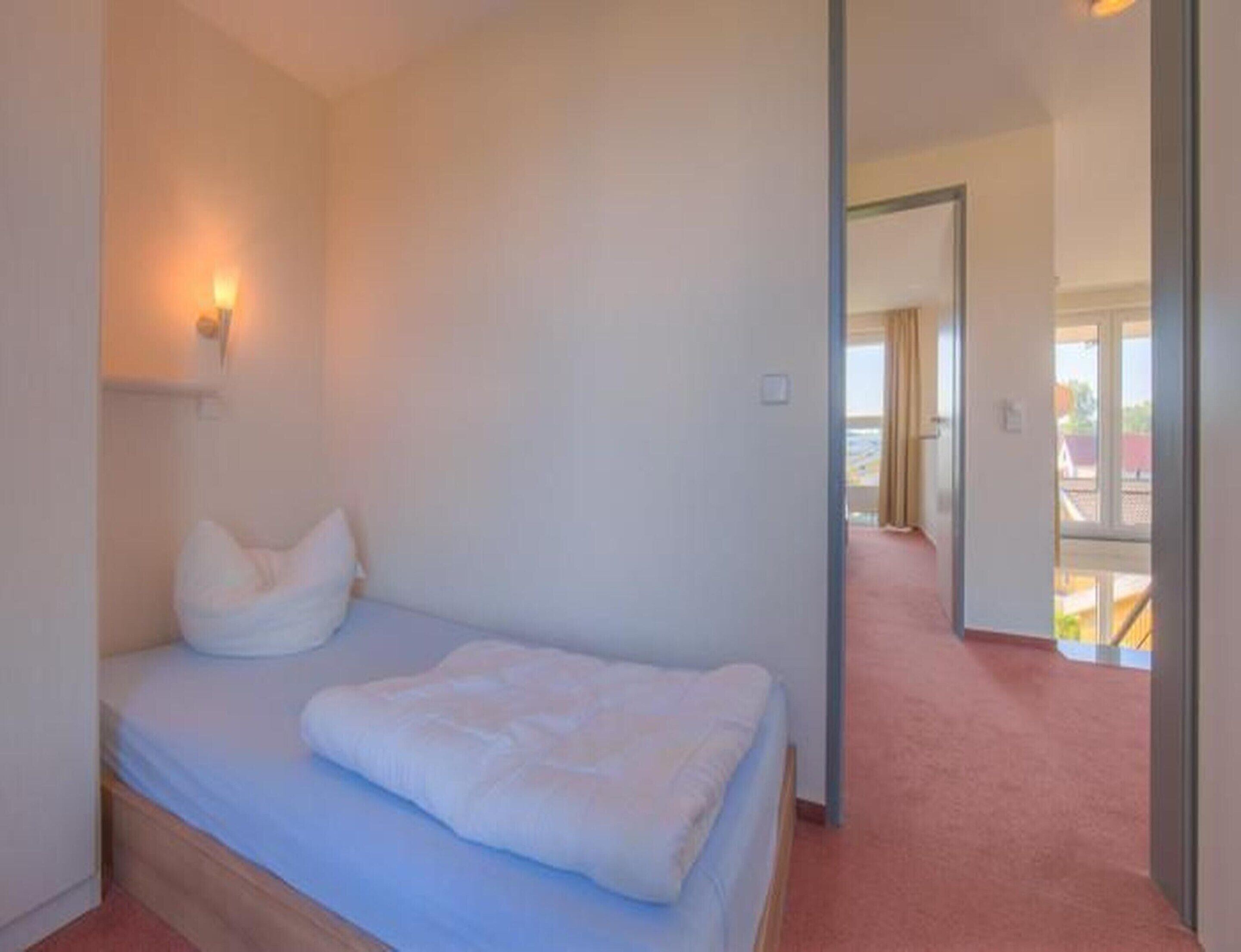 Un dormitorio con cama, una lámpara de pared y vistas por una puerta abierta.