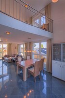 Amplia sala de estar con mesa de comedor, sillas y sofá. Tiene un balcón con barandilla y vistas al exterior.