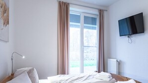 A hotel room with two beds, a TV mounted on the wall, and a window with curtains. - Schone Ferienwohnungin Rechlin (Rechlin)